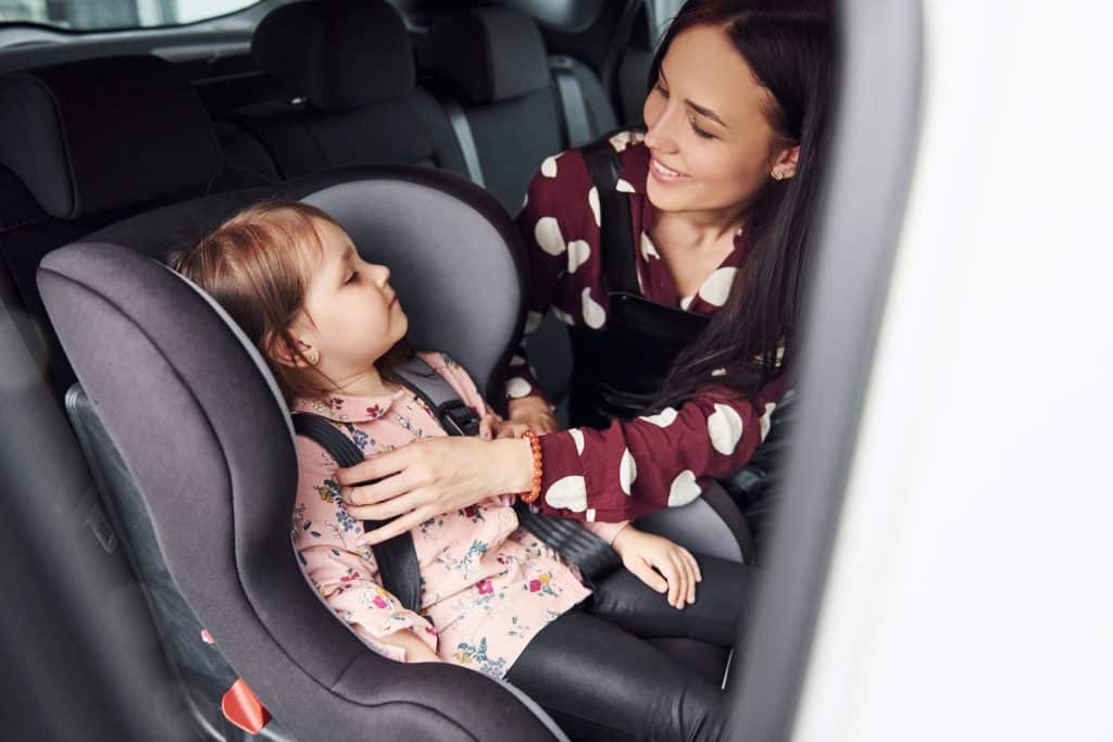 Une mère installe sa fille dans un siège auto dans les règles de l'Art.