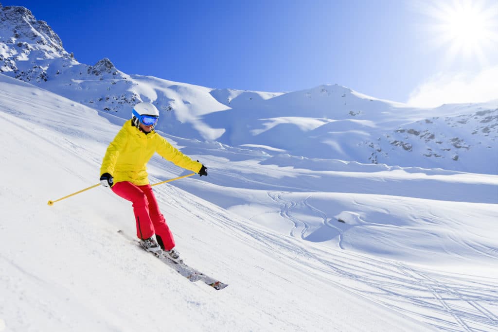 Une femme dévale une pente enneigée habillée de vêtements de ski écolo.