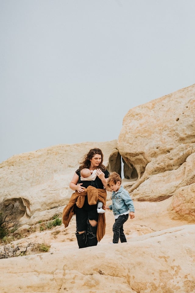 Mère avec bébé en écharpe et jeune enfant sur un terrain rocheux désertique