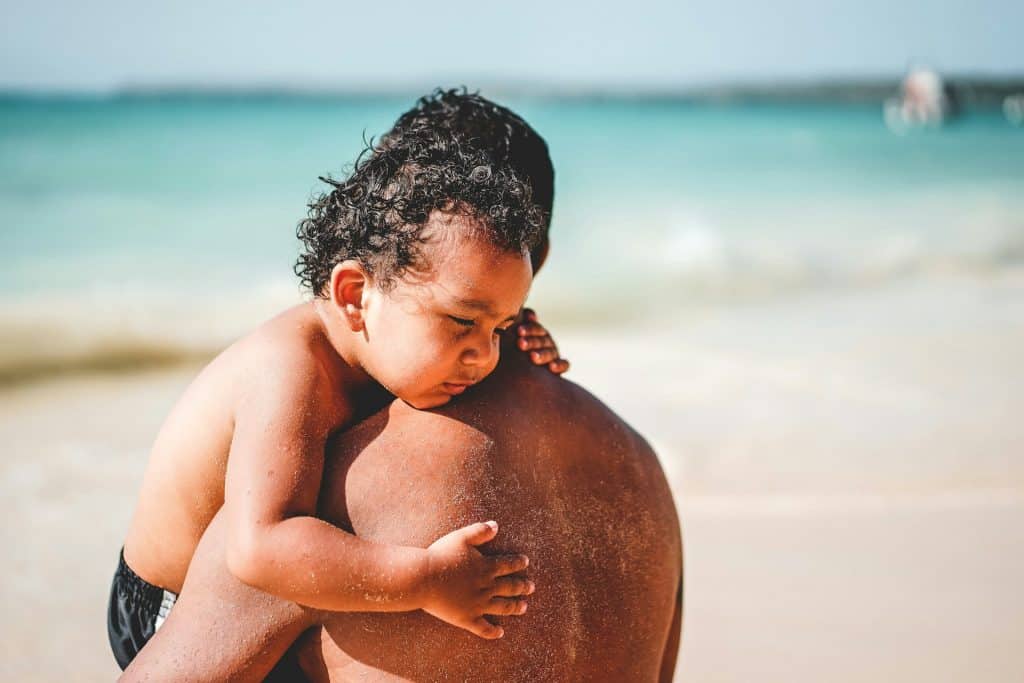 Père portant son enfant endormi sur une plage tropicale